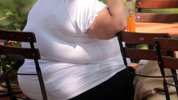 Eine extrem übergewichtige Person sitzt auf einem Gartenstuhl.