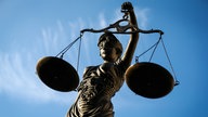 Figur der Justitia mit Waage und Augenbinde vor blauem Himmel