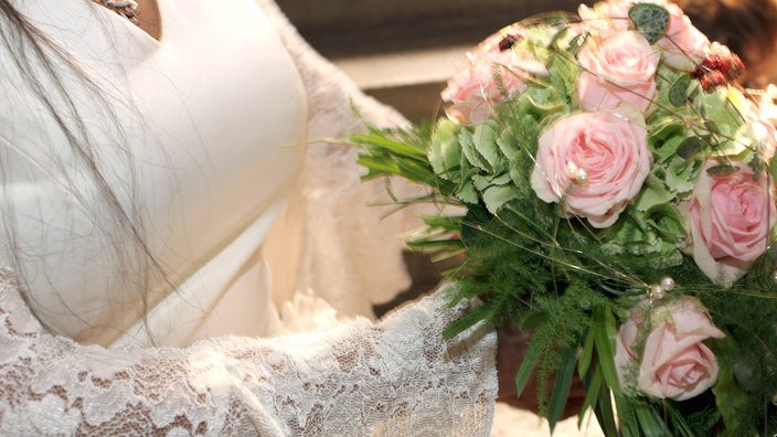 Braut in weißem Kleid hält einen Brautstrauß aus rosafarbenen Rosen in der Hand