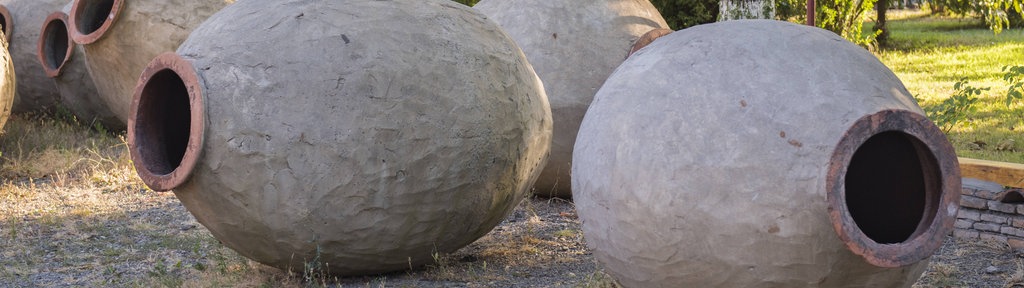 In einem Garten liegen mehrere große Tongefäße, sogenannte Quevris, die in Georgien zur traditionellen Weinherstellung verwendet werden.