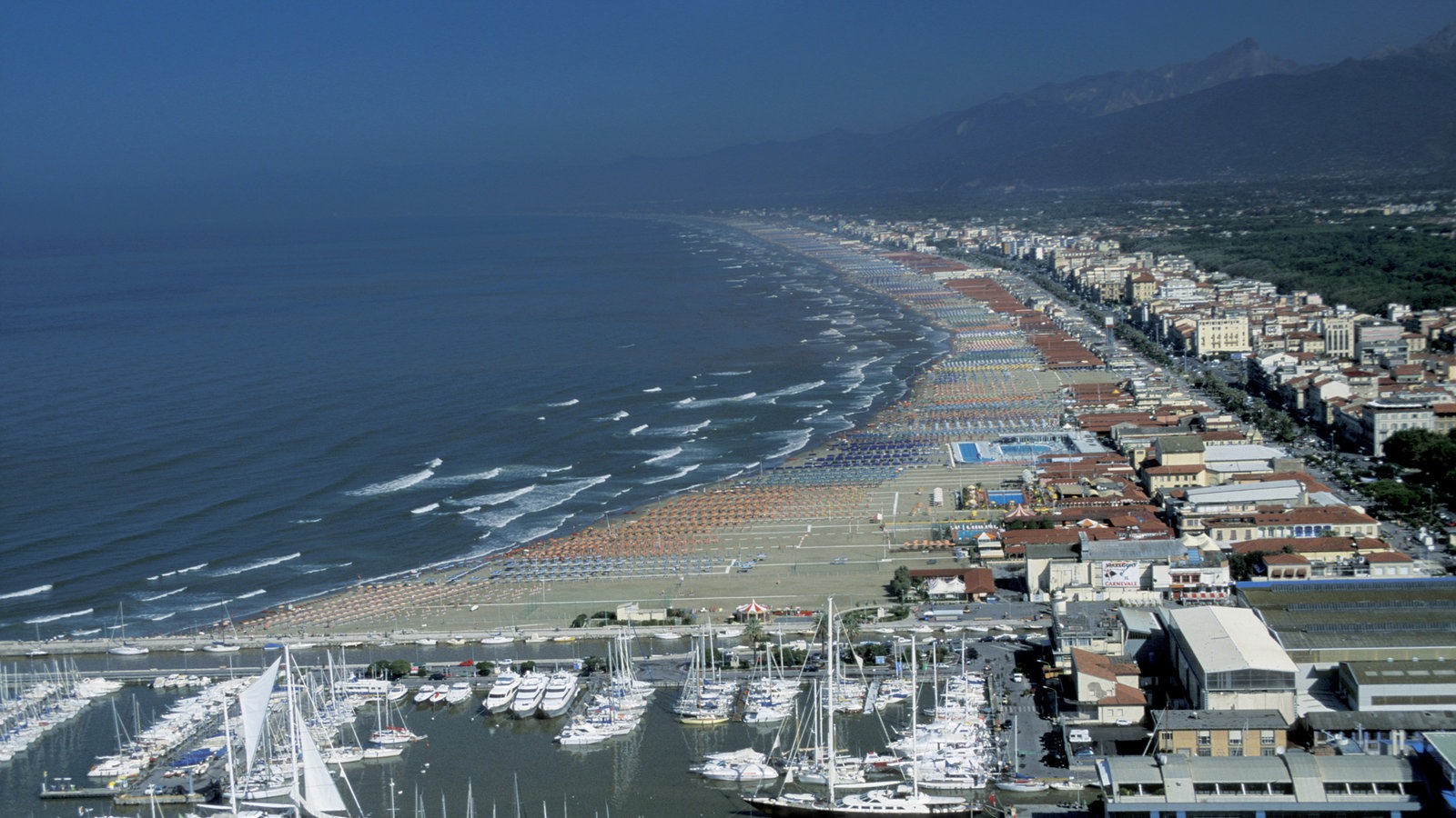 Blick von oben auf einen Jachthafen und direkt an den Strand angrenzende Hotelbauten