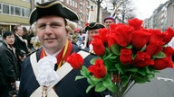 Ein Mann auf dem Rosenmontagszug hält eine Strauß Rosen in der Hand