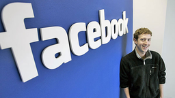 Der Gründer von Facebook, Mark Zuckerberg, lehnt in der Zentrale seines Unternehmens an einer blauen Wand. Über ihm steht in weißen Buchstaben das Wort Facebook.